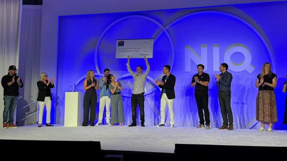 Damian Gayler holding the $250,000 Culture Slam winner's cheque on stage with NIQ colleagues